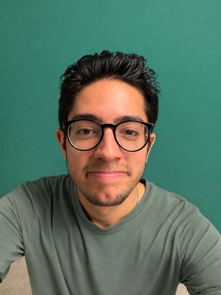 Portrait of Parsa Abbasian, smiling, wearing glasses and a sage green t-shirt against a teal studio background